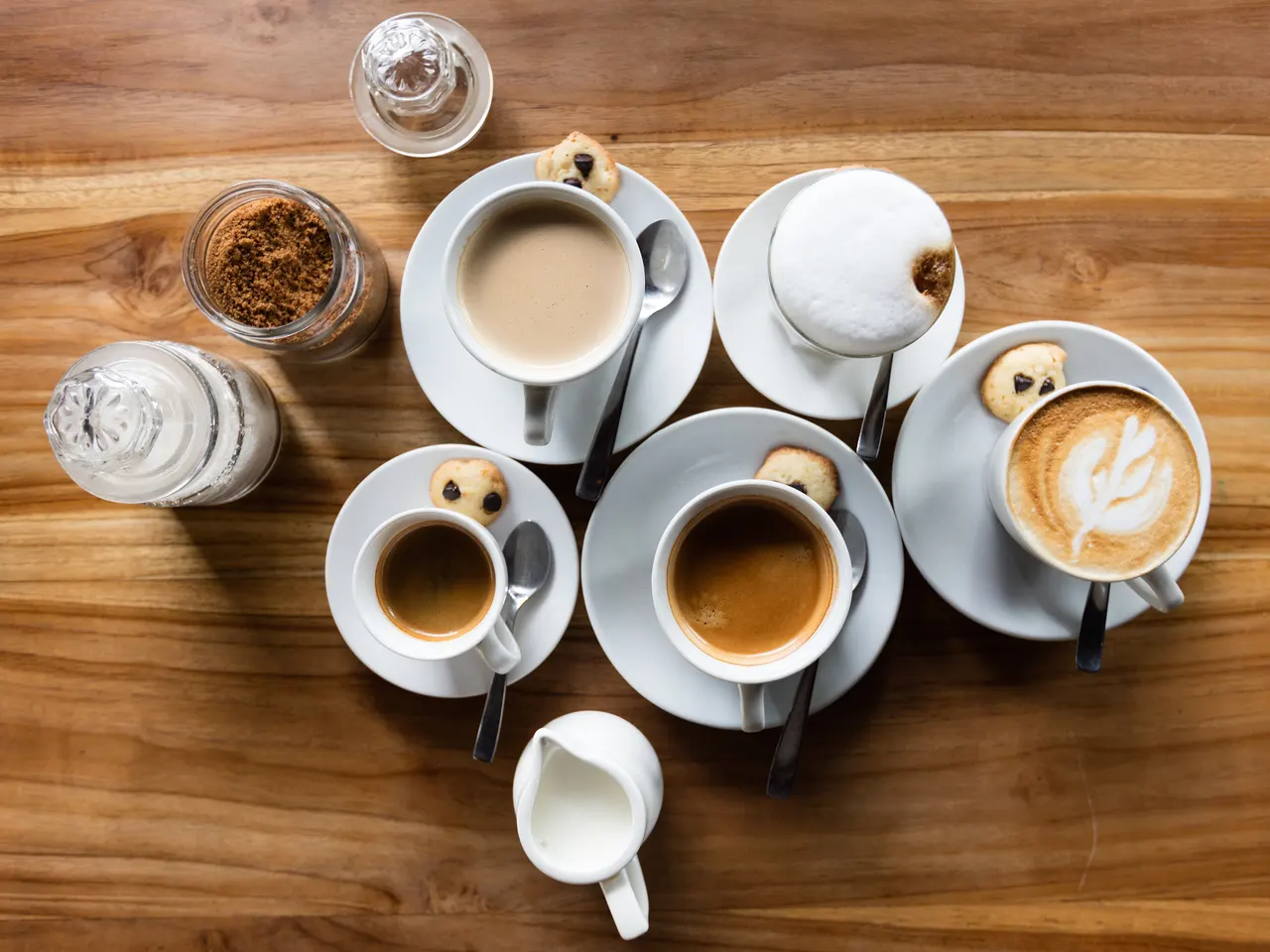 Overhead view of espresso, cappuccino and latte cups with biscuits on a wooden cafe table in Canggu, Bali.