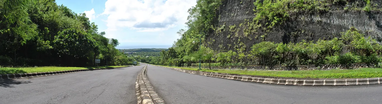Empty asphalt road on the Bukit peninsula in Bali curving downhill past a limestone cliff towards the sea.