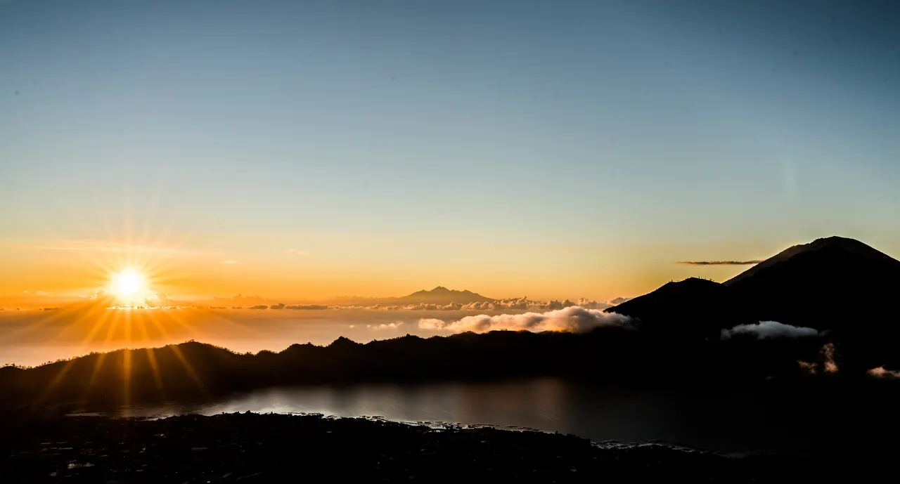 Sunburst over Lake Batur at dawn with the volcanic ridge of Mount Batur silhouetted in Bali.
