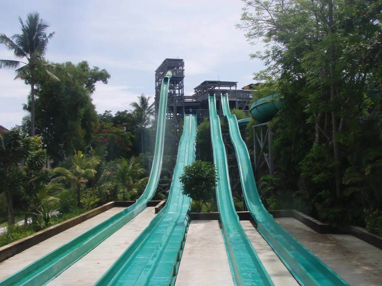 Two turquoise racer water slides running down through palms and tropical greenery at Waterbom Park, Kuta, Bali.