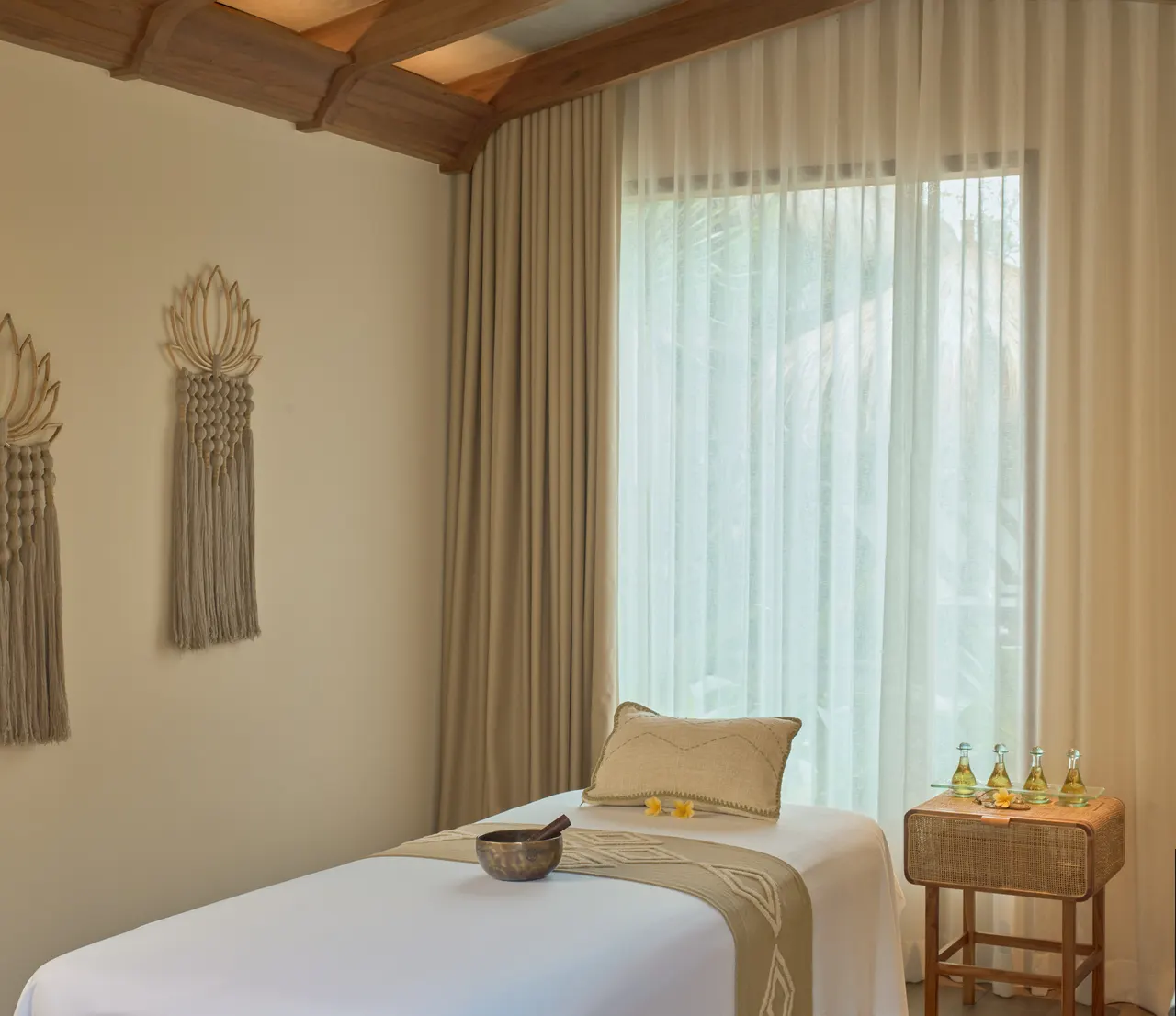 Balinese spa treatment room with a massage table, woven wall art and sheer curtains softening the daylight.