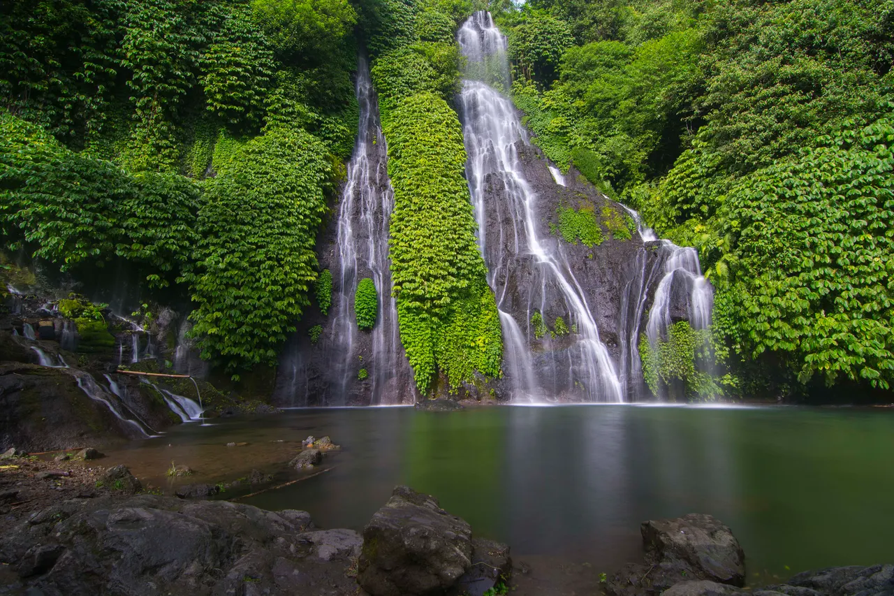 Banyumala twin waterfall in northern Bali falling down a jungle-covered rock face into a still green pool.